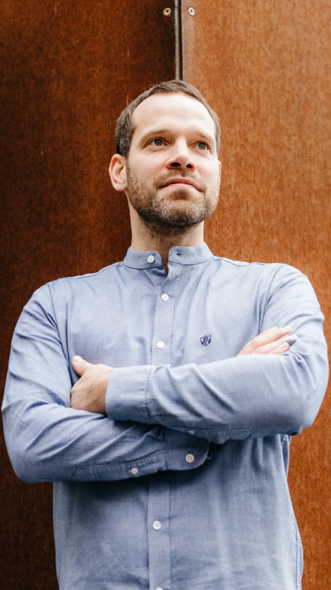 Das Bild zeigt Dennis Ahrens lächelnd und mit verschränkten Armen vor einer rostigen Fassade.