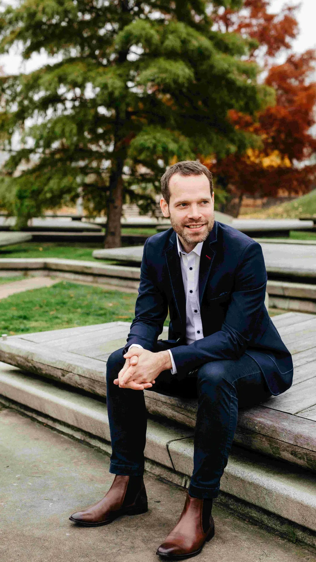 Das Bild zeigt Dennis Ahrens in einem Park sitzend und freundlich lächelnd.