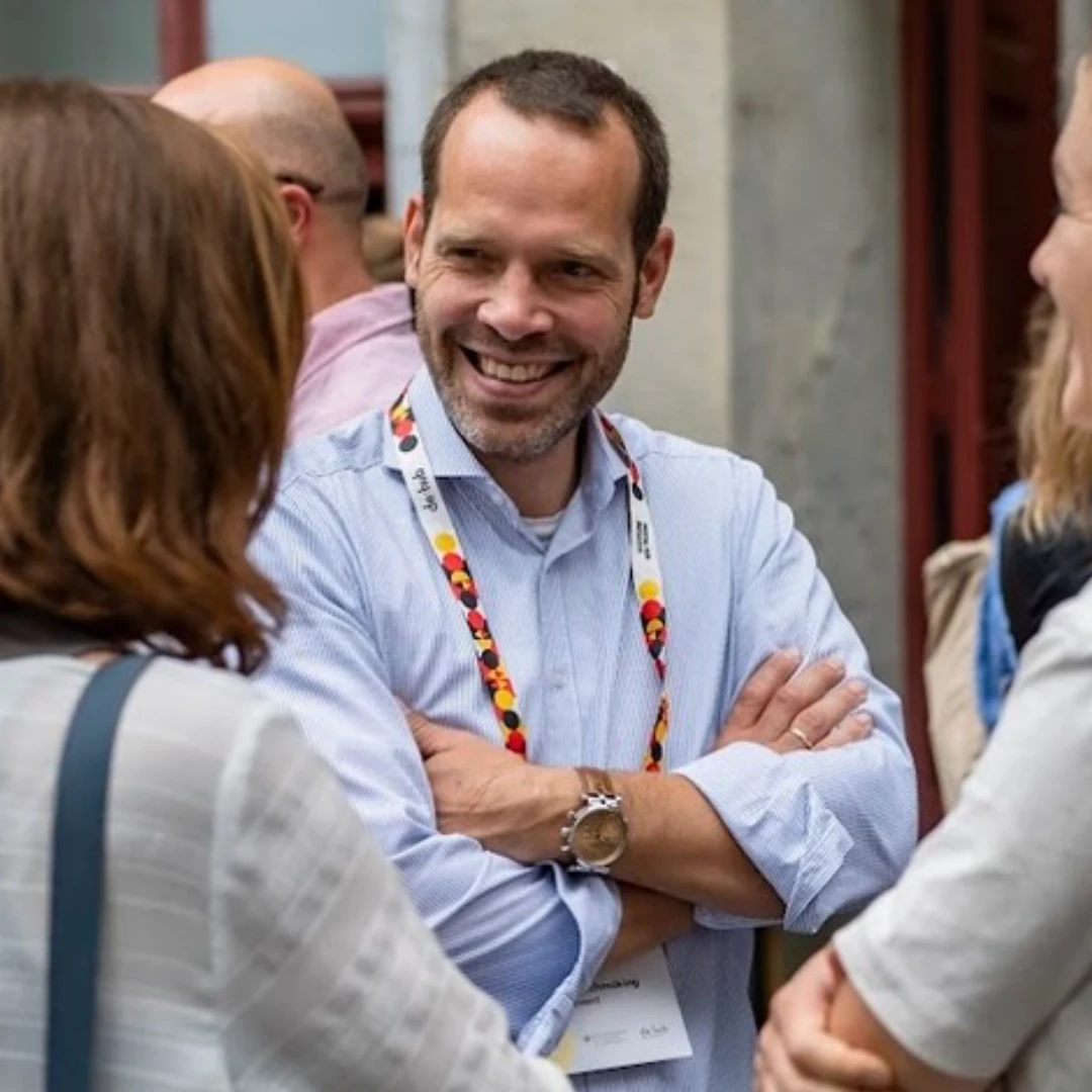 Das Bild zeigt Dennis Ahrens im Gespräch mit zwei Menschen. Im Hintergrund sind weitere Personen sichtbar.